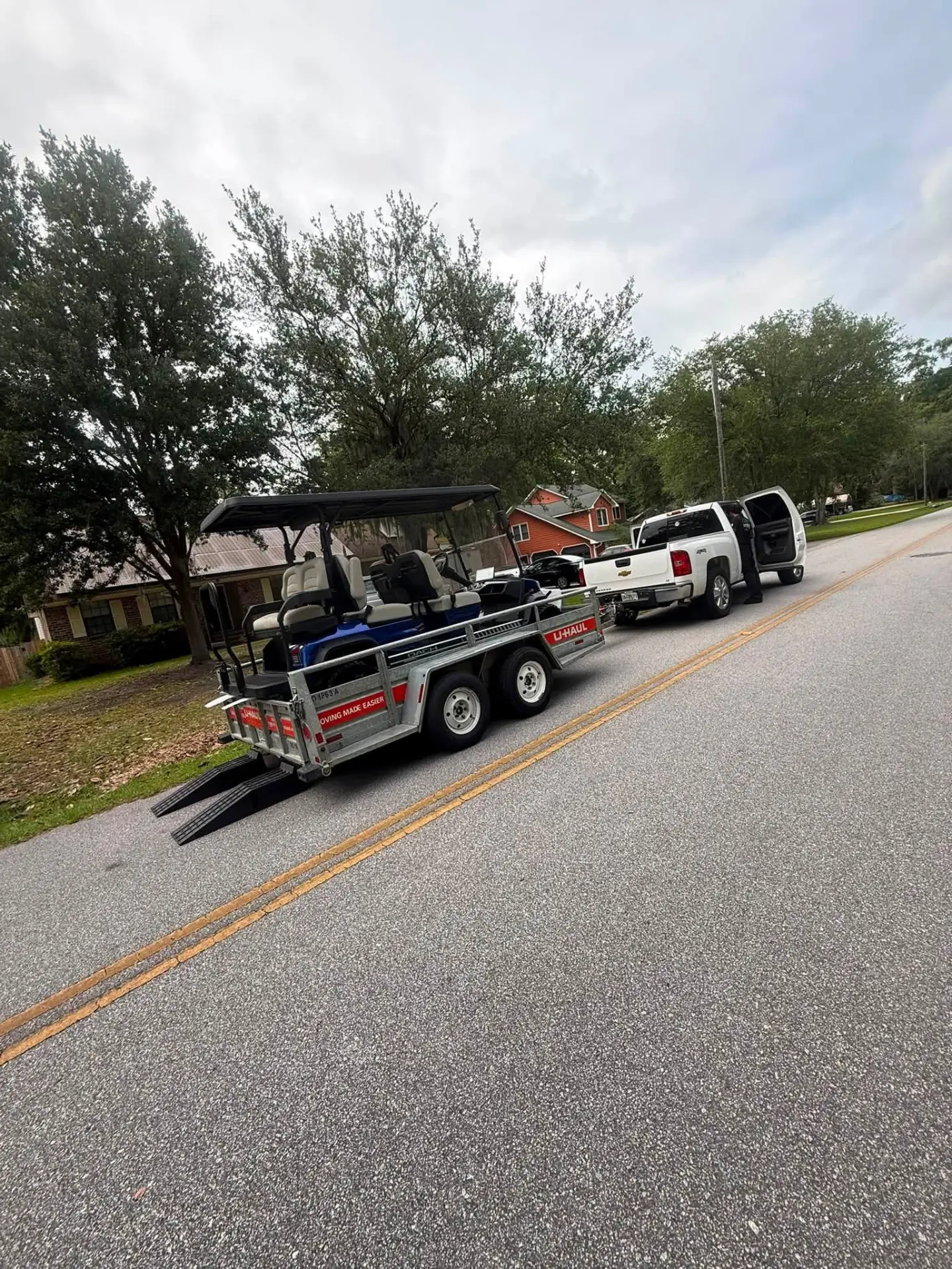Golf cart loaded on a U-Haul trailer being towed by a pickup truck